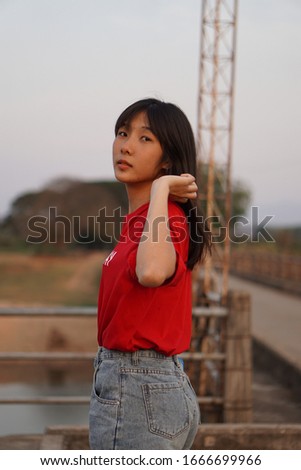 A cute female teenager is wearing a red T-shirt with the word "SATURDAY" and wearing jeans. She is waiting for someone
