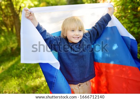 Portrait of cute little boy in public summer park with russian flag on background. Fans child supporting and cheering theirnational team. Day of independence. Pride and patriotism.