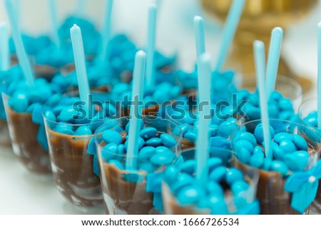 Close up of chocolate pudding brown into cup plastic with blue spoon isolated on white background with shallow depth of field. Chocolate sweets served at a birthday party. Selective focus.