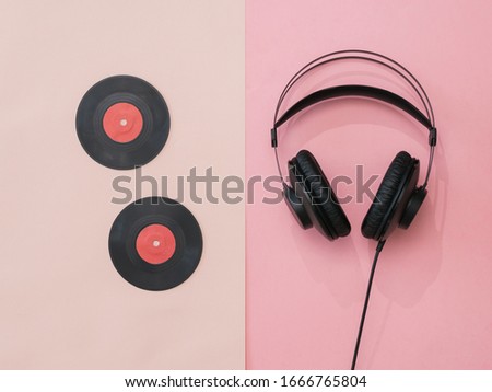 Two vinyl discs and headphones on a pink background. Retro technique for playing music.