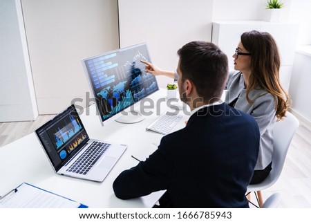 Two Businesspeople Examining Graph On Computer At Workplace