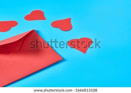 Red paper hearts near postal envelope on blue background. Love message. Concept of Valentines Day. Space for text