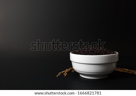 Thai black rice berry in a white ceramic bowl on black background.