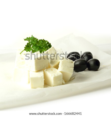 High key image of a block of fresh Feta cheese with black olives and parsley garnish on grease-proof paper against a white background. Copy space. Royalty-Free Stock Photo #166682441