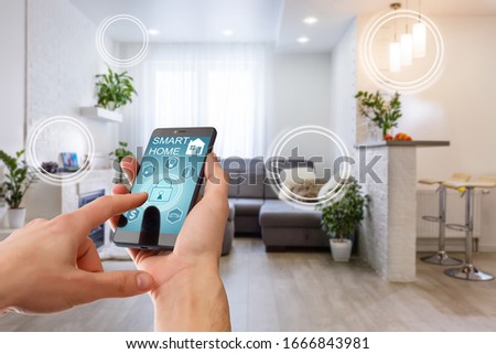 Smart home technology interface on smartphone app screen with augmented reality (AR) view of internet of things (IOT) connected objects in the apartment interior, person holding device Royalty-Free Stock Photo #1666843981
