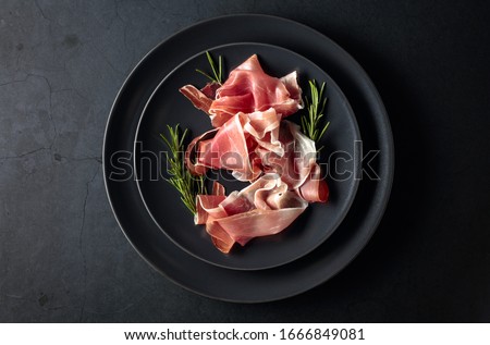 Prosciutto and rosemary on a black plate. Top view, copy space. Royalty-Free Stock Photo #1666849081