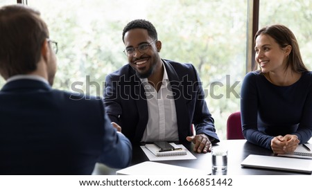 Smiling African American male employee shake hand of colleague greeting getting acquainted at office meeting, happy diverse businessman handshake close deal after successful negotiations at briefing Royalty-Free Stock Photo #1666851442