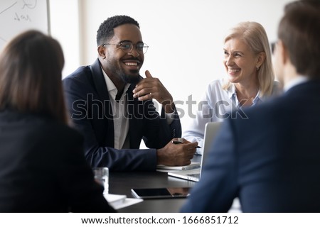 Smiling multiracial diverse businesspeople sit at office desk discussing business project together, happy multiethnic colleagues coworkers brainstorm talk consider cooperation in boardroom Royalty-Free Stock Photo #1666851712