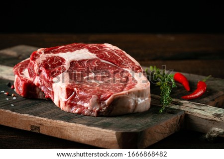 Fresh raw beef rib eye steak with red pepper and herbs on a wooden background Royalty-Free Stock Photo #1666868482