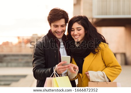 Spending Time Together. Young couple having fun carrying bags and looking at the mobile phone in the city