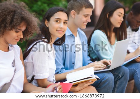 Exams Preparation. Group Of Multi-Ethnic Students Studying Together Outdoors, Selective Focus On Arabic Girl With Notepad