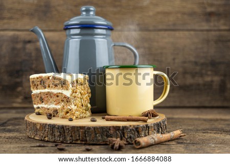A yellow tin cup of hot tea with tea pot and cake on wooden table.