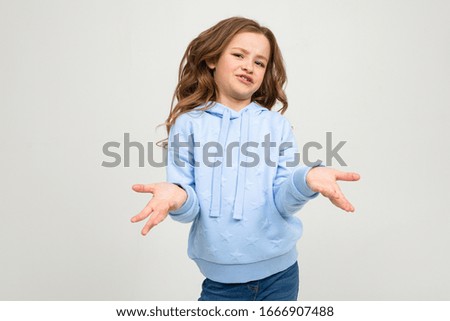 dissatisfied teenager girl in a blue hoodie indignantly waving hands on a light studio background