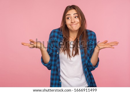 Don't know answer! Portrait of funny confused girl in checkered shirt shrugging shoulders with clueless embarrassed expression, having doubts, not sure. indoor studio shot isolated on pink background Royalty-Free Stock Photo #1666911499