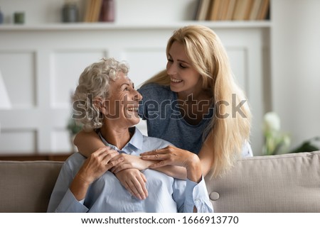 Overjoyed senior 60s mother and adult daughter relax together in living room hugging and cuddling, happy mature mum and grownup girl embrace show love enjoy home family weekend together Royalty-Free Stock Photo #1666913770