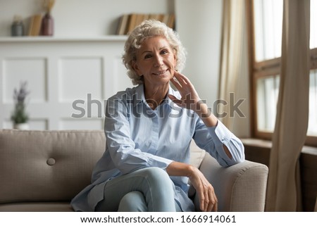Portrait of happy mature 60s grandmother sit on couch in living room look at camera posing, smiling senior 70s woman rest on sofa at home, enjoy leisure weekend spend in retirement house