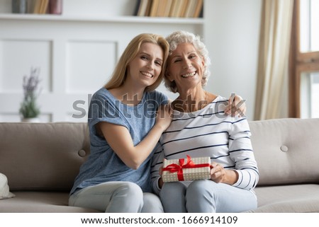 Portrait of happy adult daughter greeting excited senior mom make birthday surprise present gift package, smiling mature mother and grownup girl child celebrate anniversary at home together