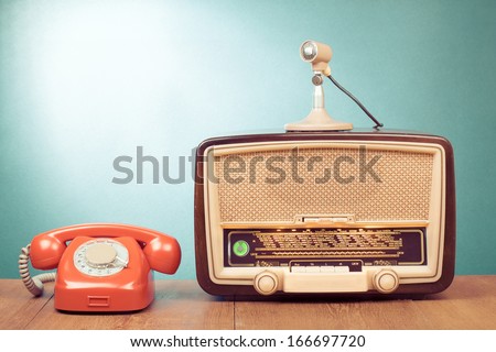 Retro radio with green light, microphone and telephone on wooden table