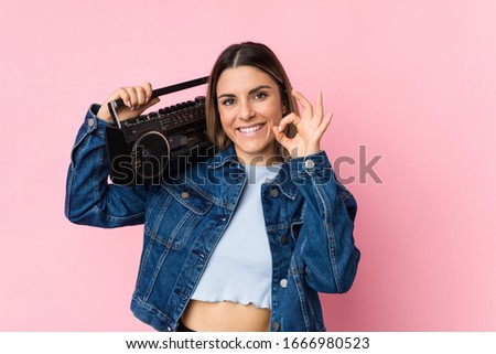 Young caucasian woman holding a guetto blaster cheerful and confident showing ok gesture.