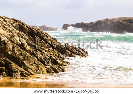 Beach in winter with dramatic cloudy sky, strong wind and waves breaking against the cliffs, San Juan de la Canal beach, Costa Quebrada, Spain