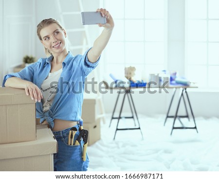 Happy young woman taking selfie while smiling cheerfully, having moved into a new flat