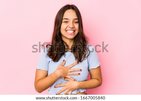 Young mixed race hispanic woman isolated laughs happily and has fun keeping hands on stomach.