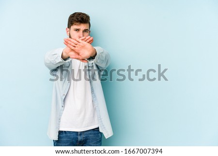 Young caucasian man isolated on blue background doing a denial gesture