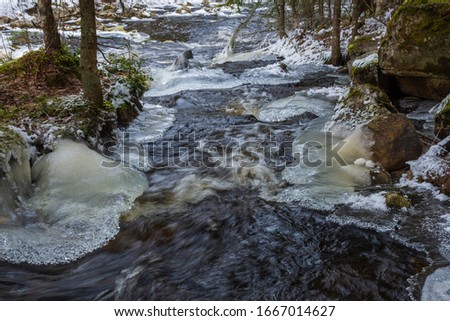 Stream in a forest with whirling water and ice in beautiful shapes on both sides, picture from Mellansel Vasternorrland, Sweden.