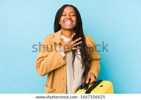 Young african american traveler woman holding a suitcase isolated laughs out loudly keeping hand on chest.