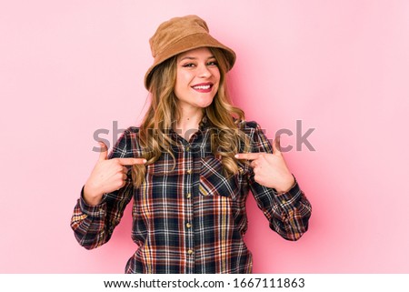 Young caucasian woman wearing a hat isolated surprised pointing with finger, smiling broadly.