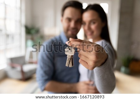 Focus on keys, held by excited young spouses homeowners. Happy married family couple celebrating moving in new house home , demonstrating keys, standing in apartment, real estate mortgage concept. Royalty-Free Stock Photo #1667120893