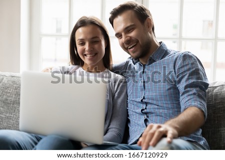 Happy married couple relaxing on comfortable sofa, watching funny video on computer. Excited smiling spouses laughing on comedian movie, enjoying spending free weekend leisure time together at home. Royalty-Free Stock Photo #1667120929