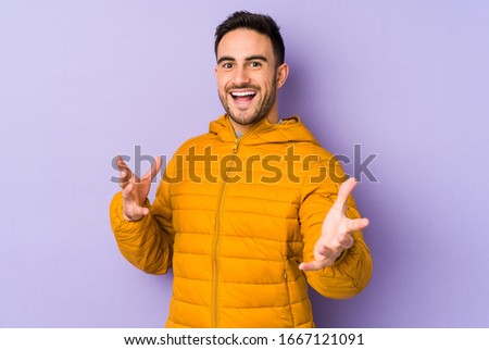 Young caucasian man isolated on purple background feels confident giving a hug to the camera.
