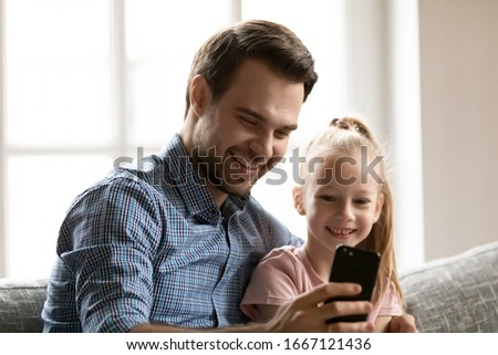 Head shot close up smiling dad taking selfie photo on mobile phone with cute little child daughter, resting together on comfy sofa. Happy parent showing funny videos, stories in social network to kid.