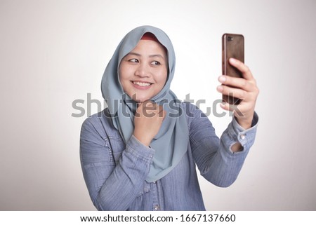 Portrait of muslim woman wearing hijab smiling and taking selfie picture photograph of her self on smart phone