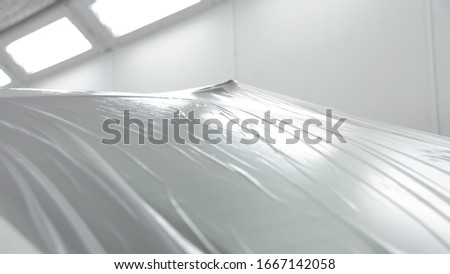 White car is standing in a spray booth covered with a transparent film. Ready to paint Royalty-Free Stock Photo #1667142058