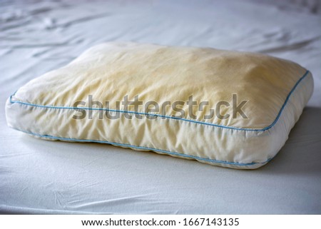 Old dirty used yellow sweat stained sleep pillow on a mattress. Condition of the pillow used for a long time. 