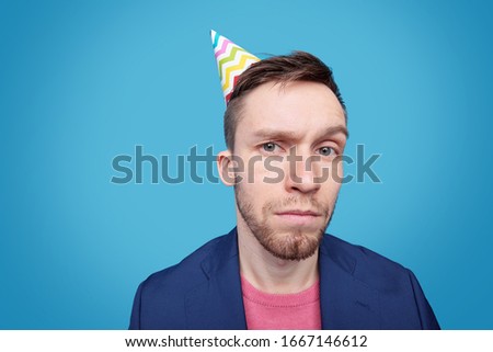 Suspicious young man in jacket, pullover and birthday cap looking at you in isolation against blue background