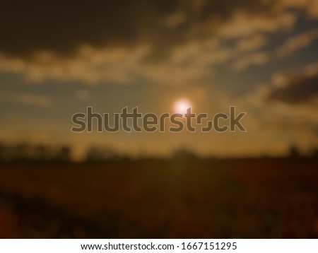 Backlit natural background with sun, sky and fields at twilight that is an out of focus image which is a blur style picture.