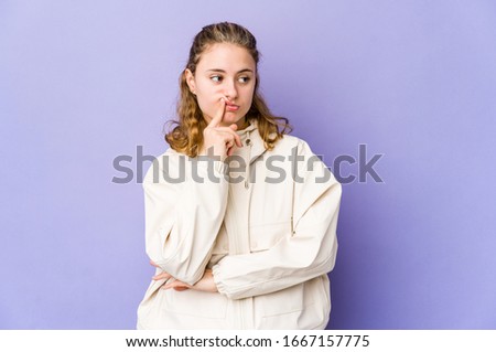 Young caucasian woman on purple background looking sideways with doubtful and skeptical expression.