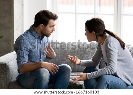 Stressed young married family couple arguing emotionally, blaming lecturing each other, sitting on couch. Depressed husband quarreling with wife, having serious relations communication problems. Royalty-Free Stock Photo #1667160103