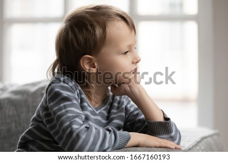 Head shot side view thoughtful little child boy sitting alone on comfy sofa, putting head on hand. Close up stressed unhappy small kid feeling loneliness lack of parents attention, looking away. Royalty-Free Stock Photo #1667160193