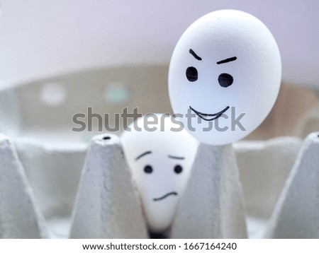 Two white chicken eggs with a sad and cheerful emoji sit in a box