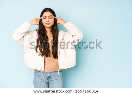 Young indian woman on blue background focused on a task, keeping forefingers pointing head.