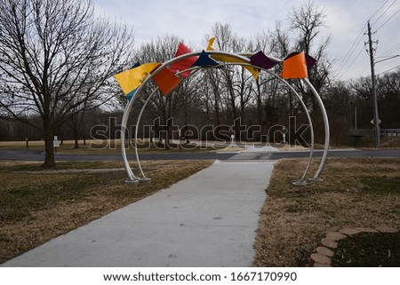 Colorful archway over a sidewalk in a park. A crosswalk is behind it. Picture taken in Gladstone, Missouri.