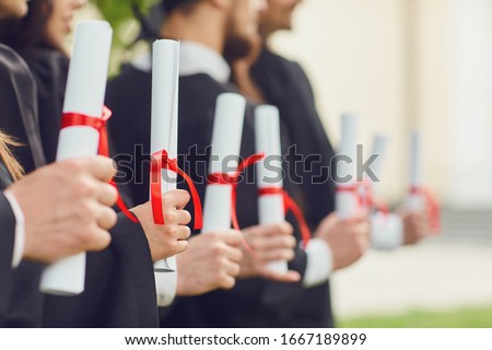 Scrolls of diplomas in the hands of a group of graduates. Royalty-Free Stock Photo #1667189899