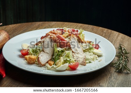 Caesar salad with croutons, parmesan, bacon, chicken, egg in black plate on wooden background. Restaurant serving. Close up with copy space. Close up