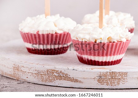 Strawberry ice cream popsicle lollies with whipped cream frozen in muffin molds on gray background.  Royalty-Free Stock Photo #1667246011