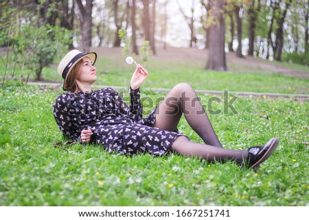 blonde girl in a straw hat with a dandelion in his hand lies  on the grass in the spring garden. Spring season concept.