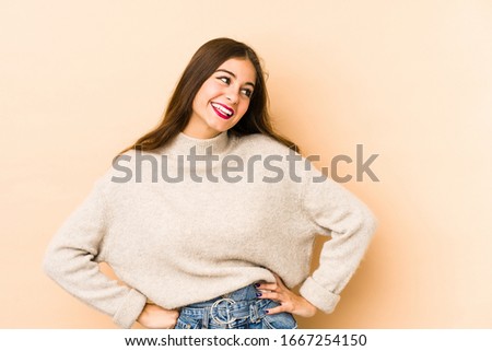 Young caucasian woman isolated en beige background confident keeping hands on hips.